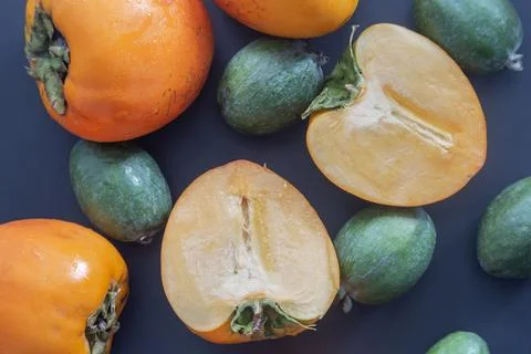 Macro flat lay of fresh sliced persimmons and green feijoa fruits background Stock Photos