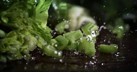 Macro of fresh celery pieces fall with splashing water drops on wooden table Stock Footage 268991635