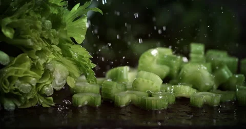 Macro of fresh celery pieces fall with splashing water drops on wooden table Stock Footage 268992078