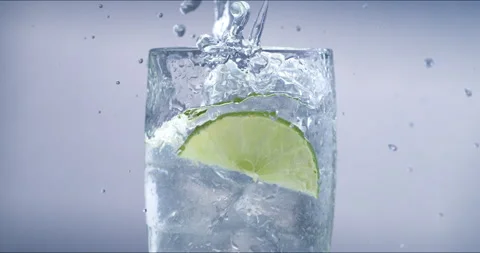 Macro of fresh green lime fruit slice falls in transparent glass with water Stock Footage 268469694