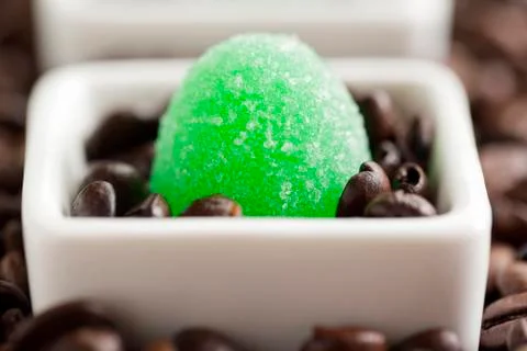 Macro image of green candy and coffee beans in coffee cup. Stock Photos