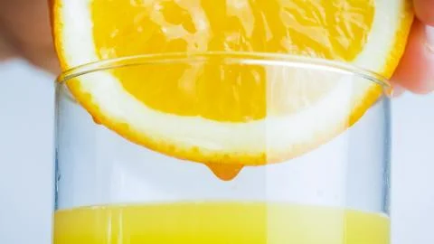 Macro image of persons hand squeezing fresh juice from orange half in glass Foto stock