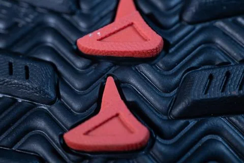 A macro image showing a black rubber shoe sole with angular red tread inserts. Stock Photos