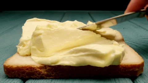 MACRO: Large piece of butter is spread with a knife on bread Stock Footage 174555046