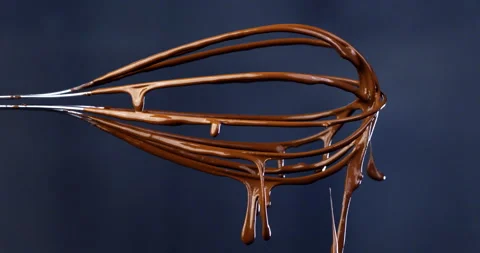 Macro of liquid dark cocoa chocolate cream falls from metal mixing whisk Stock Footage 268422189