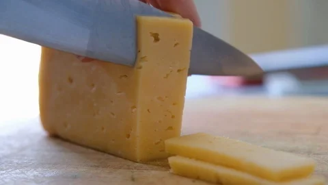 Macro of a middle aged chef cutting cheese with knife on wooden board, close up Stock Footage 111864120