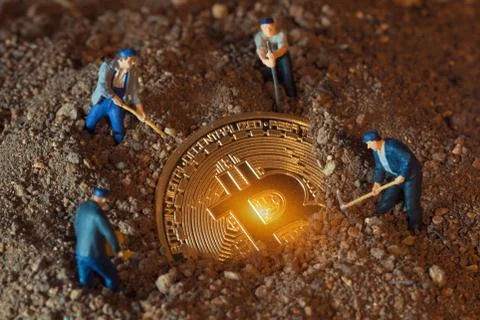 Macro miner figurines digging ground to uncover big shiny bitcoin Stock Photos