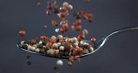 Macro of mixed peppercorn seeds falling down silver spoon on dark background Stock Footage 268979613