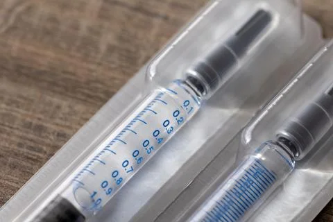 A macro portrait of a package with two syringes in it lying on a wooden table Stock Photos
