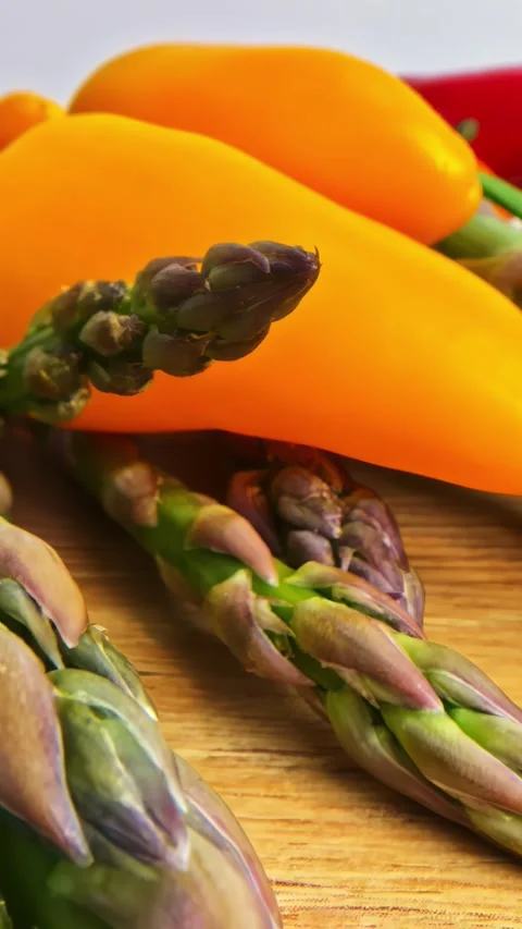 Macro Pull-back of Fresh Asparagus Spears and Colorful Sweet Peppers on Wooden Stock Footage 336241270