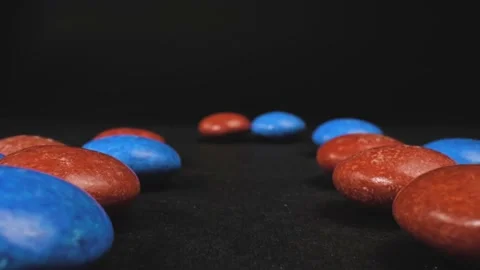 Macro push in shot of button-shaped red and blue candy with a black Video stock 229913389