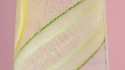 Macro rotation captures cucumber ribbon and lemon slice in sparkling water glass Stock Footage 332468321