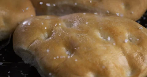 Macro of salt grains fall on hot steamy italian flatbread focaccia in bakery Stock Footage 268994793
