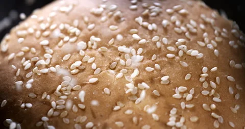 Macro of sesame grains fall on soft fresh burger bun in artisan bakery Stock Footage 268994728