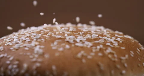 Macro of sesame grains fall on soft fresh burger bun in artisan bakery Stock Footage 268994815