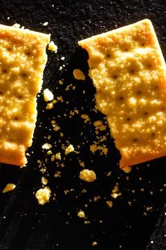 Macro Shot of Broken Wheat Cracker with Scattered Crumbs on Black Backgroun.. Fotos de archivo