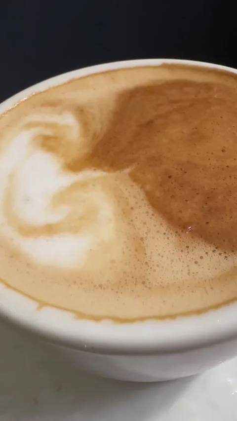 Macro shot of cup with hot foam coffee on roasted coffee beans, vertical orie Stock Footage 330106550