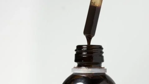 Macro shot of dripping liquid from a dropper into bottle Stock Footage 246708034