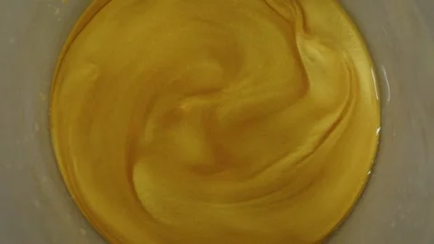 Macro shot of a gold-colored liquid with gold flakes swirling in a container Stock Footage 291870814