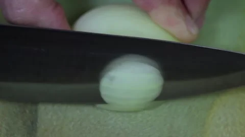 A macro shot of a man's hand with a knife cutting half an onion on a table. Video stock 155888482
