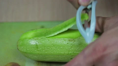 Macro shot of a man's hand that peels zucchini with a vegetable peeler Stock Footage