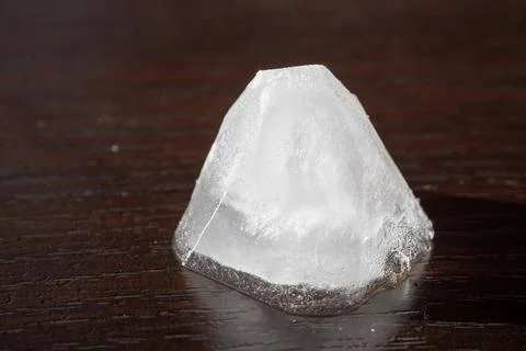 Macro shot of a melting ice cube standing on a dark wooden surface Stock Photos