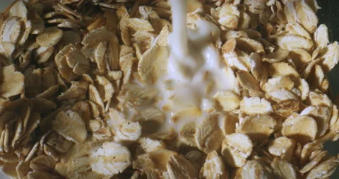 Macro shot of milk being poured into bowl of rolled oats. Healthy choice for Video stock 149254147