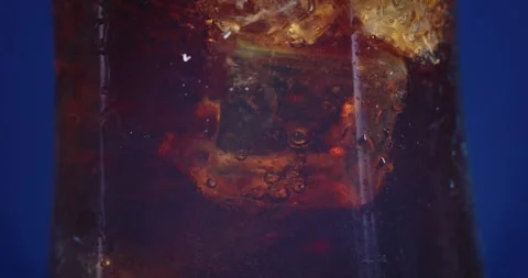 Macro shot of pouring cola drink into glass. Ice cubes inside. Video stock 246148023