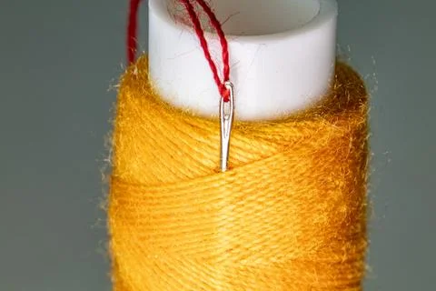 Macro shot of a red thread passing through a sewing needle eye with yellow .. Stock Photos