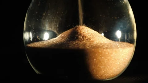 Macro shot of sand flowing through hourglass timer against dark background .. Stock Footage 334595181
