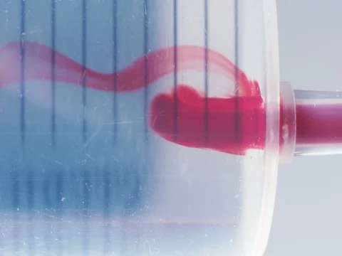 Macro shot of syringe pulling red liquid into saline solution against white Vídeo Stock 72575213