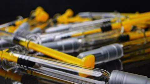 Macro shot of syringes on a reflective black surface. The camera moves slow.. Video stock 303499096