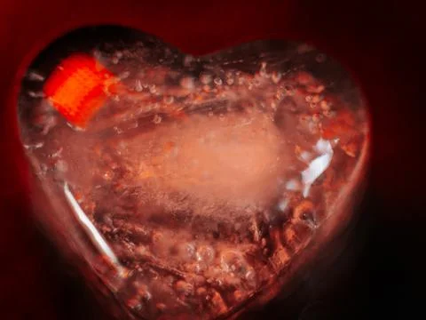 Macro shot of two heart-shaped ice cubes melting on a red surface. Stock Photos