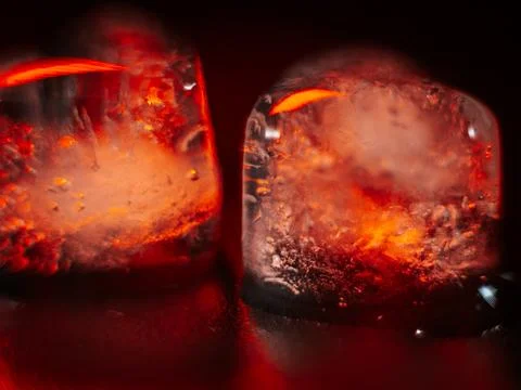 Macro shot of two heart-shaped ice cubes melting on a red surface. Stock Photos