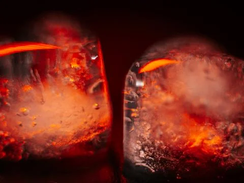 Macro shot of two heart-shaped ice cubes melting on a red surface. Stock Photos