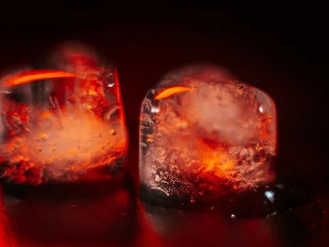 Macro shot of two heart-shaped ice cubes melting on a red surface. Stock Photos