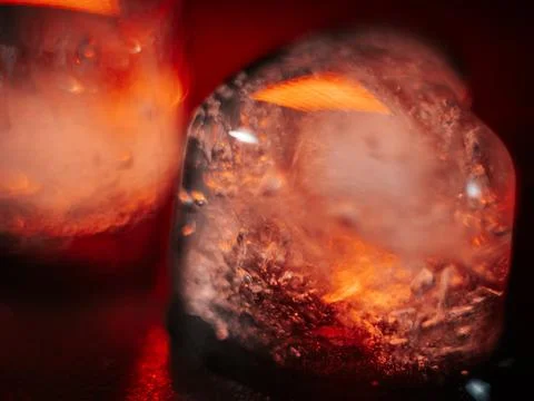 Macro shot of two heart-shaped ice cubes melting on a red surface. Stock Photos