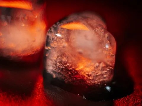 Macro shot of two heart-shaped ice cubes melting on a red surface. Stock Photos