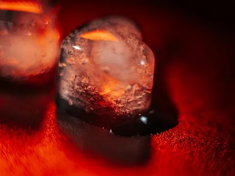 Macro shot of two heart-shaped ice cubes melting on a red surface. Stock Photos