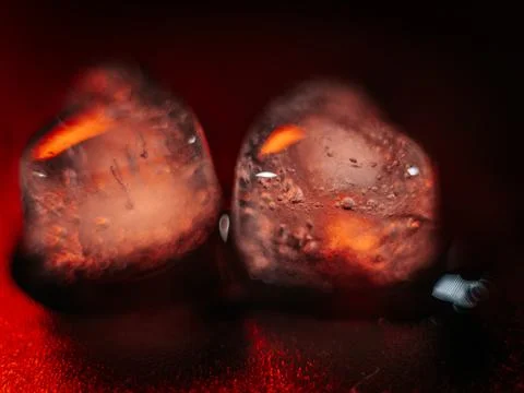 Macro shot of two heart-shaped ice cubes melting on a red surface. Stock Photos