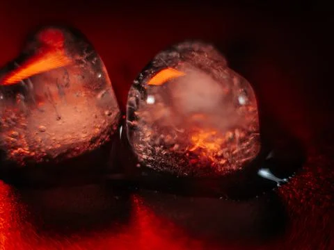 Macro shot of two heart-shaped ice cubes melting on a red surface. Stock Photos