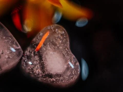 Macro shot of two heart-shaped ice cubes melting on a red surface. Stock Photos