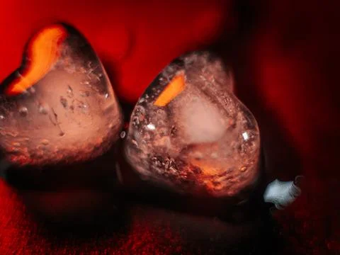 Macro shot of two heart-shaped ice cubes melting on a red surface. Stock Photos