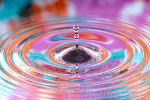 Macro shot of a water drop creating ripples on a colorful, abstract surface 스톡 사진