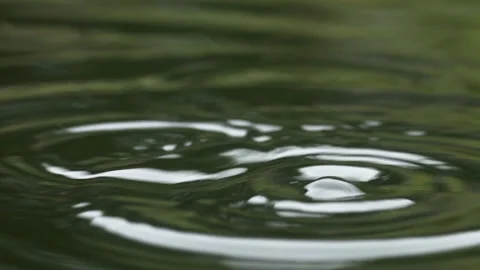 Macro shot of water droplets falling in slow motion into a clear pool Stock Footage