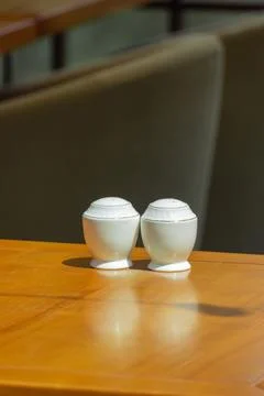 Macro shot of white ceramic salt and pepper shakers on wooden table in rest.. Stock Photos