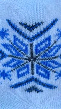 Macro shot of white knitted wool texture with a blue snowflake ornament as a  Stock Photos