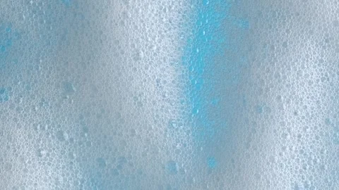 Macro shot of white soap suds flowing down window glass on blue background... Stock Footage 269326280