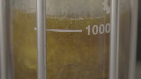 Macro shot of yellow liquid mixing in an industrial glass reactor 스톡 동영상 327633501