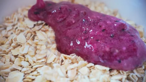 Macro slow motion close up of blended blueberry puree spreading over oats, .. Video stock 329843908